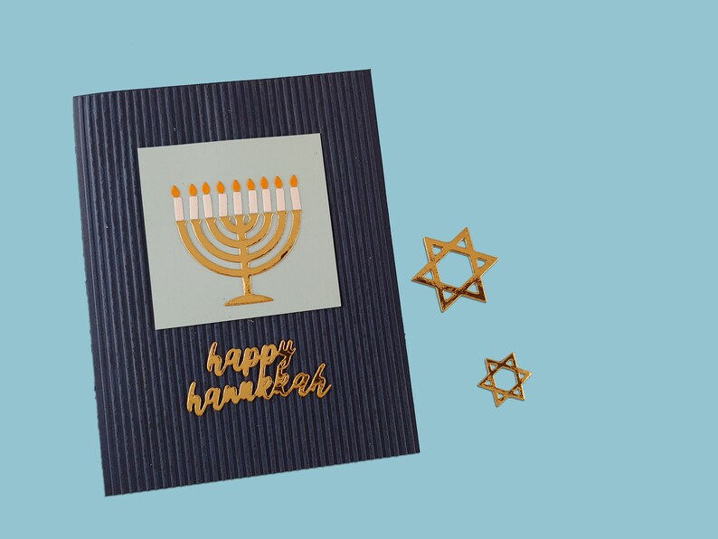 May include: A blue card with a gold menorah and the words "happy hanukkah" on it. There are two gold Star of David stickers on the blue background.