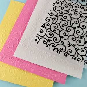 May include: Three sheets of paper with an embossed swirl pattern. The top sheet is clear plastic with a black swirl pattern. The bottom sheet is yellow, the middle sheet is pink, and the top sheet is white.