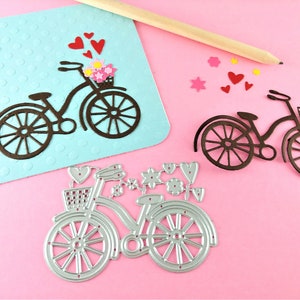 May include: Two metal die-cut bicycle shapes, one brown and one silver, with flowers and hearts. The brown bicycle has a basket with flowers. The silver bicycle has a basket and a heart.