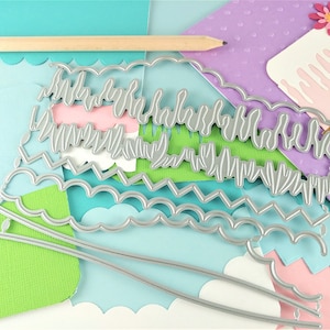 May include: A set of metal die cuts for crafting. The die cuts are shaped like layers of a cake with different decorative edges. The die cuts are on a background of colorful paper.