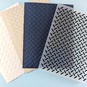May include: A collection of textured paper sheets in various colors, including white, beige, navy blue, and translucent. Each sheet features a repeating diamond plate pattern, creating a tactile and industrial aesthetic. The sheets are arranged on a light blue surface.