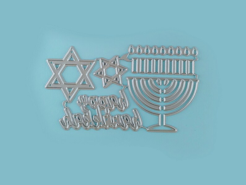 May include: Silver metal die cut design featuring a menorah, two Star of David shapes, and the words "Happy Hanukkah".