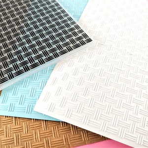 Peut inclure: Quatre tapis d'embossage texturés différents, un noir, un blanc, un bleu clair et un or. Chaque tapis a un motif tissé.