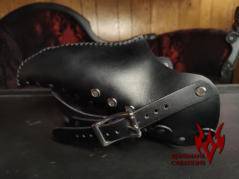 Puede incluir: Collar de cuero negro con detalles en metal plateado y cierre de hebilla. El collar est&aacute; cosido con un borde decorativo. El texto "Runemane Creations" es visible en la esquina inferior derecha.