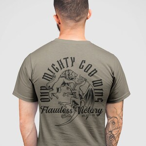 Könnte beinhalten: Ein grünes T-Shirt mit einem schwarzen Motiv eines Löwen, der gegen einen Drachen kämpft. Das Motiv ist umgeben von dem Text "Our Mighty God Wins" und "Flawless Victory 66:2017-10".