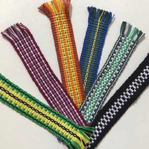 May include: Seven woven bookmarks with fringe ends in various colors and patterns, including green, yellow, black, white, red, orange, blue, and purple.