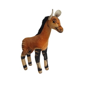 May include: A vintage plush okapi toy. The okapi has a brown body with black and white striped legs. It has a black mane, small horns, and tan ears. The toy is standing on a white background.