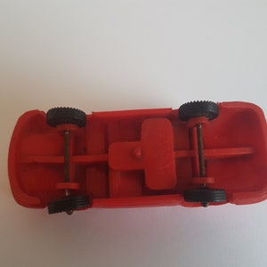 May include: Red toy car with black wheels and a metal axle. The car is upside down, showing the underside of the chassis.