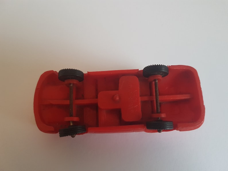May include: Red toy car with black wheels and a metal axle. The car is upside down, showing the underside of the chassis.