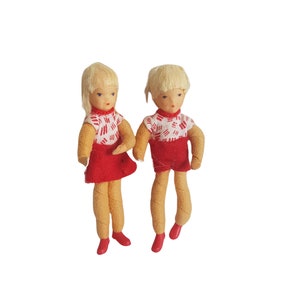 May include: Two small dolls with blonde hair wearing red and white clothing. The dolls are made of fabric and have painted faces.