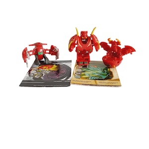 May include: Two red Bakugan toys with their corresponding cards. The Bakugan are in their open, ball form. The cards are brown with white text and images of the Bakugan.