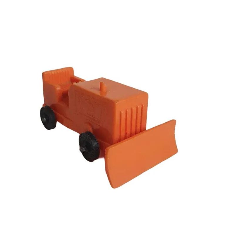 May include: Orange toy bulldozer with black wheels and a front blade. The toy has a rectangular body with a small seat and a vertical grill design on the front. A small peg is on top.