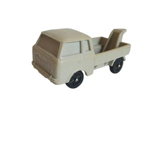 May include: A light gray toy truck with a flatbed and a tow hook. The truck has black wheels and a black grill.