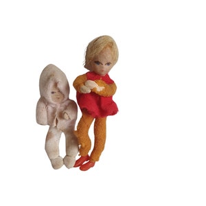 May include: Two handmade fabric dolls, one wearing a red dress and the other wearing a white hooded jacket. Both dolls have blonde hair and blue eyes.
