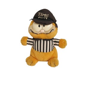Könnte beinhalten: Orangefarbener Garfield Plüschtier, das eine schwarz-weiße Schiedsrichteruniform mit einem schwarzen Hut trägt, auf dem "Time Out" steht.