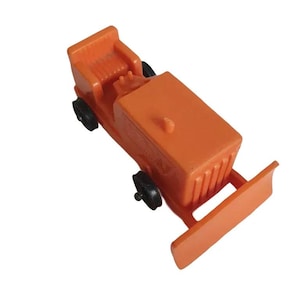 May include: An orange toy bulldozer with black wheels and a front blade. The toy has a rectangular body with a small seat and a raised section on top. The blade is flat and angled downwards.