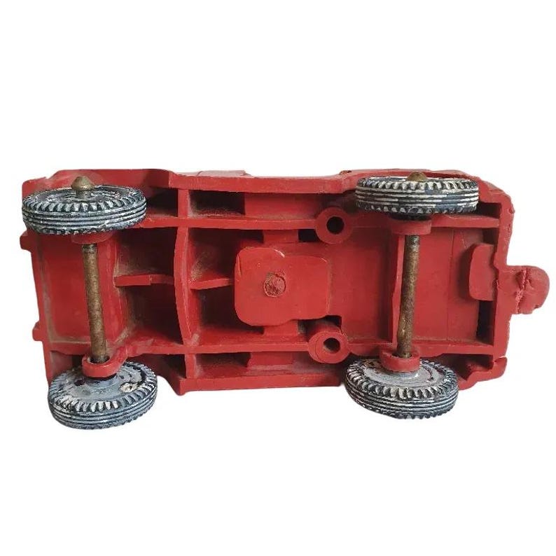 May include: Red toy truck with four black wheels, viewed from the underside. The truck has a detailed underside with visible axles and a moulded plastic body.