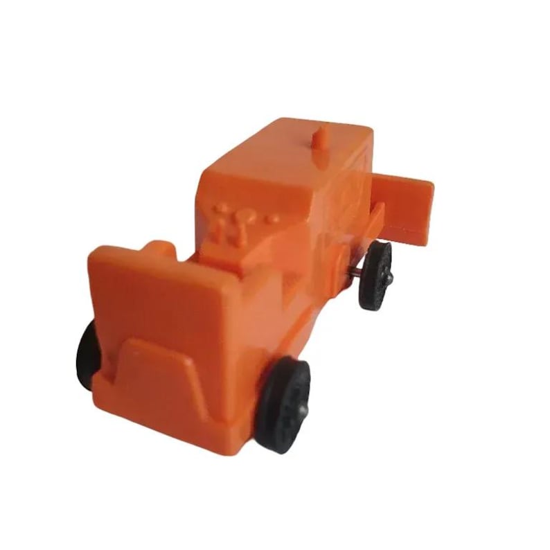 May include: An orange toy truck with black wheels. The toy has a rectangular body with a front bumper and a small, rectangular extension on the side. The wheels are small and black.