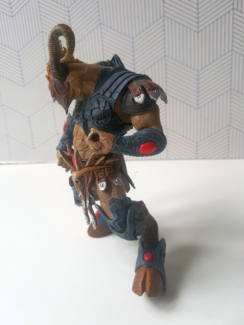 May include: A brown and gray action figure of a horned creature wearing armor. The figure has red accents on its armor and is posed in a dynamic stance.