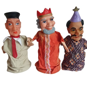 May include: Three hand puppets, one wearing a red crown and orange robe, one wearing a purple and white patterned robe and a blue star hat, and one wearing a beige shirt and a red tie.