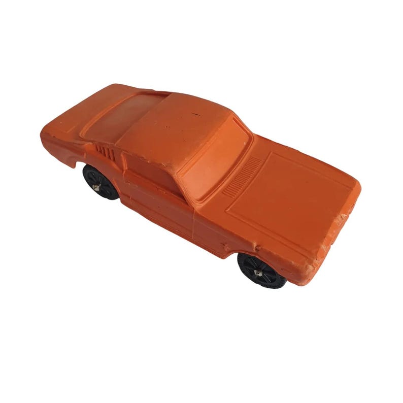 Puede incluir: Coche de juguete naranja con ruedas negras. El coche de juguete tiene un dise&ntilde;o cl&aacute;sico, con un cap&oacute; largo, una l&iacute;nea de techo definida y una carrocer&iacute;a rectangular. Las ruedas son visibles sobre un fondo blanco.