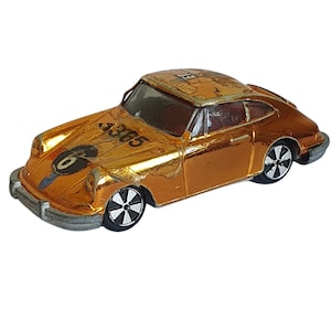 Può includere: Un'auto giocattolo dorata con ruote nere e il numero "3365" sul lato. L'auto ha una striscia da corsa nera e il numero "6" sul cofano.