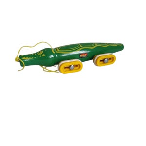 Può includere: Un coccodrillo di legno verde giocattolo con ruote gialle e una corda gialla attaccata alla testa. Il coccodrilo ha un motivo giallo e verde sulla schiena e il testo "BRIO" stampato sul lato.