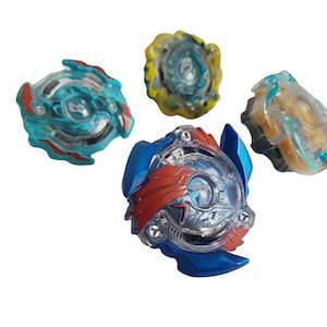 May include: Four clear plastic spinning tops with different colored accents. The tops are blue, red, yellow, and gold. The tops are designed for a game or competition.