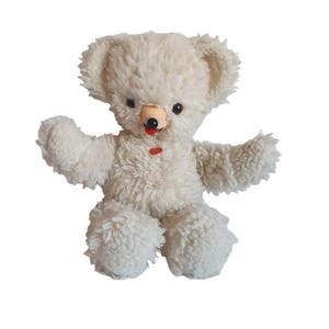 Op de afbeelding: Een vintage witte teddybeer met een pluizig, getextureerd uiterlijk. De beer heeft kleine zwarte ogen, een bruine neus en een rode tong die uitsteekt. Hij heeft een kleine rode knoop op zijn borst en poseert met uitgestrekte armen.