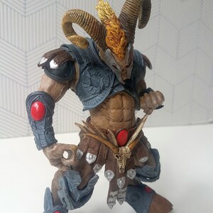 May include: A brown and gray action figure with horns, a skull belt buckle, and red accents. The figure is wearing armor and has a fierce expression.