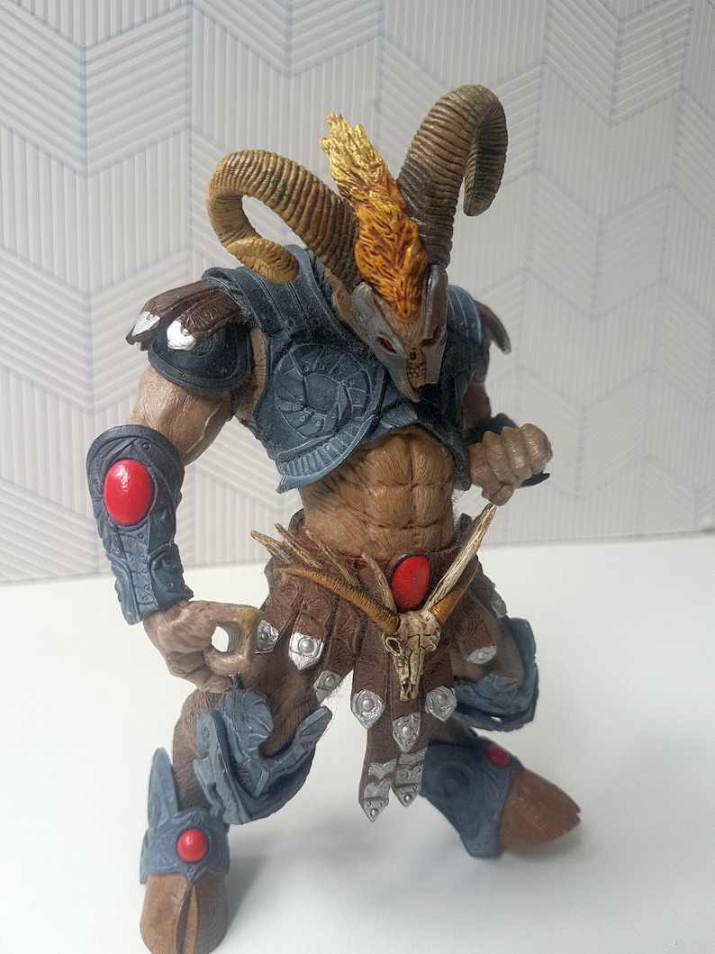May include: A brown and gray action figure with horns, a skull belt buckle, and red accents. The figure is wearing armor and has a fierce expression.