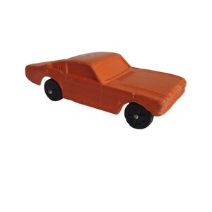Puede incluir: Un coche de juguete naranja con ruedas negras. El coche cl&aacute;sico tiene una carrocer&iacute;a coup&eacute;. El coche de juguete es de estilo vintage y est&aacute; hecho de un material s&oacute;lido. Las ruedas son negras y tienen un dise&ntilde;o sencillo.