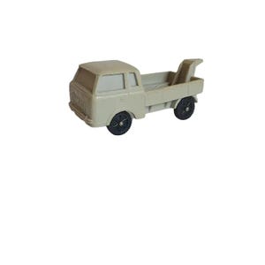 May include: A light gray toy truck with a flatbed and a black tow hook. The truck has black wheels and a white cab.