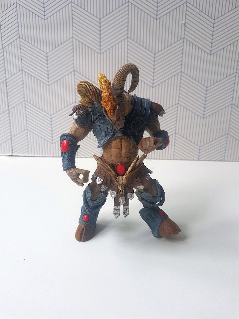 May include: A brown and blue action figure of a horned creature with a red gem on its chest. The figure is wearing a leather skirt and armor.