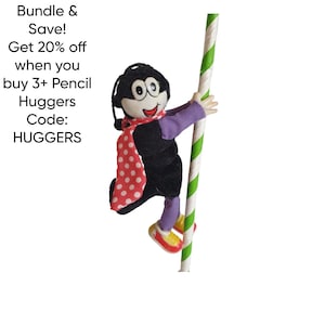May include: A plush pencil hugger doll with a black body, purple sleeves, and a red and white polka dot scarf. The doll is holding onto a green and white striped pole. Text on the left side reads "Bundle & Save! Get 20% off when you buy 3+ Pencil Huggers Code: HUGGERS."