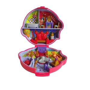 Op de afbeelding: Een roze, open, schelpvormige speelset met meerdere kamers. De binnenkant heeft een badkamer, een eethoek en een troonzaal. De kamers zijn ingericht met miniatuurmeubels en accessoires. Het speelgoed is ontworpen om op een kasteel te lijken.