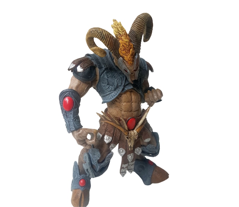 May include: A detailed action figure of a horned warrior with a red and blue armor, holding a weapon. The figure has a brown and gold horned helmet and a red gem on its chest.