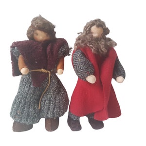 Op de afbeelding: Twee handgemaakte vilten poppen met bruin haar en baarden. De pop links draagt een bordeauxrode en grijze outfit, terwijl de pop rechts een rode en grijze outfit draagt.