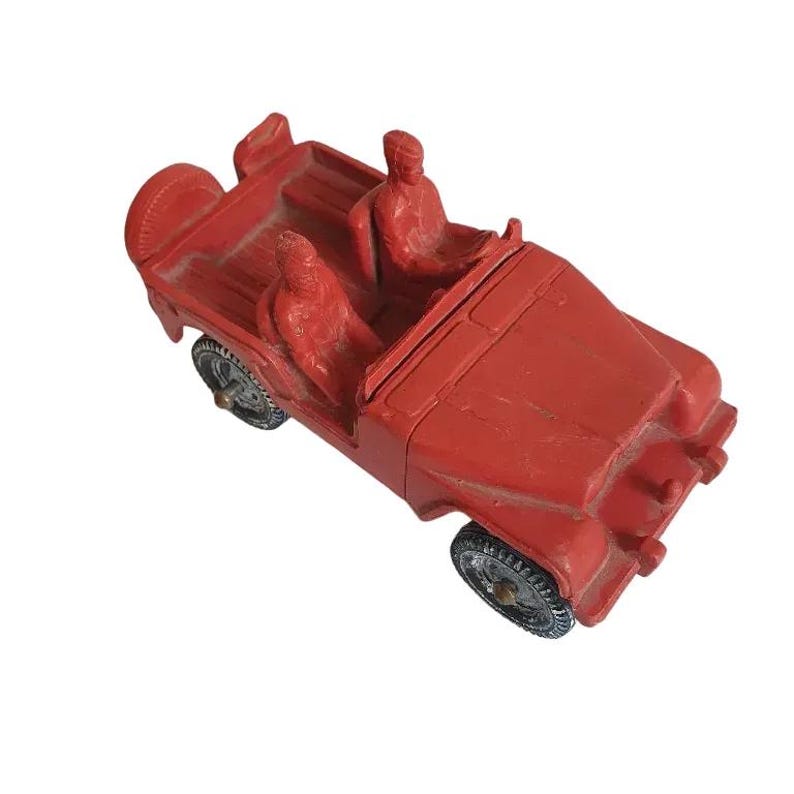 May include: Red toy jeep with two figures in the driver's seat. The jeep has a black steering wheel and black tyres.