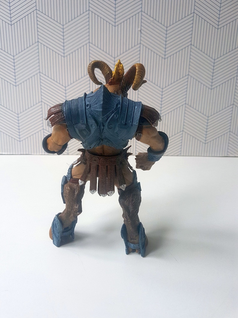 May include: A brown and blue action figure of a horned creature wearing armor. The figure has a gold crown and is standing with its arms at its sides.