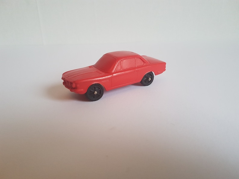 May include: A red toy car model of a classic BMW coupe. The car has black wheels and a detailed exterior.