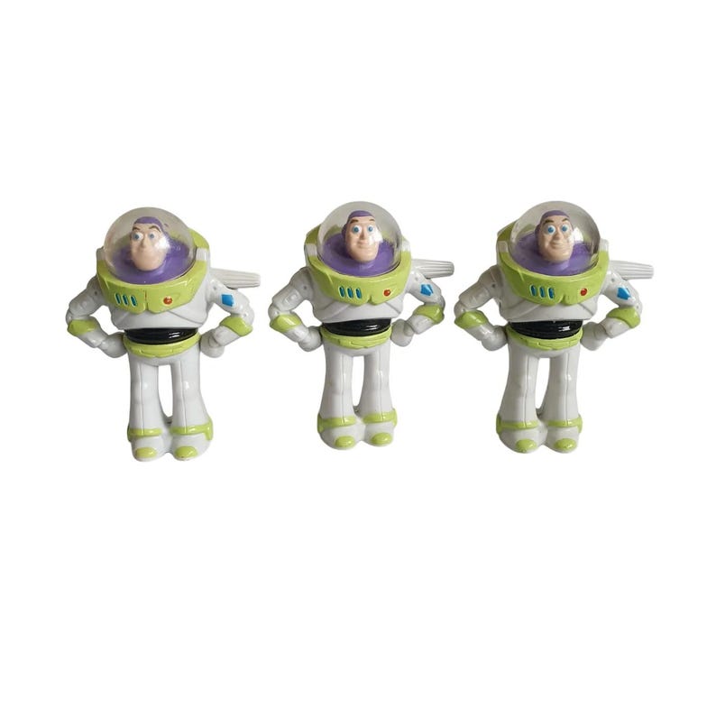 May include: Three Buzz Lightyear action figures. Each figure is white, green, and purple, with a clear helmet and wings. The figures are standing upright, with their arms at their sides. The toys are from the Toy Story franchise.