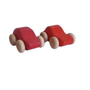 May include: Two red wooden toy cars with brown wooden wheels. The cars are side by side.