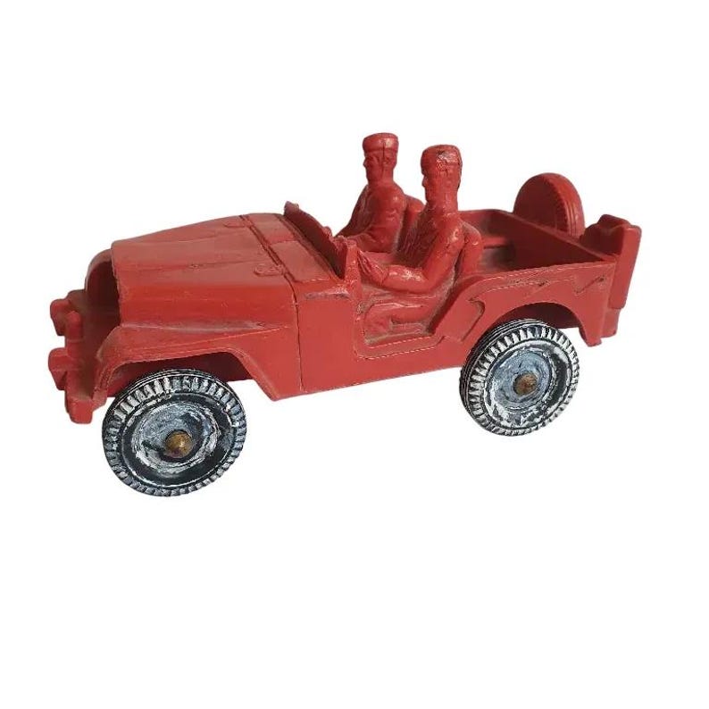 May include: A red toy jeep with two figures in the driver's seat. The jeep has white tyres and a spare tyre on the back.