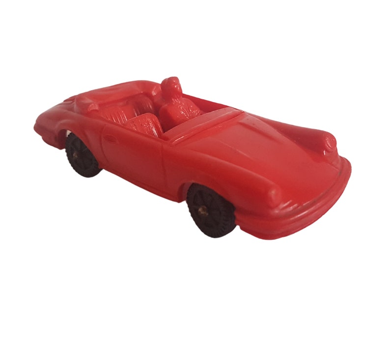 May include: A red toy car with black wheels and a black interior. The car is a convertible and has a driver and passenger in the seats.