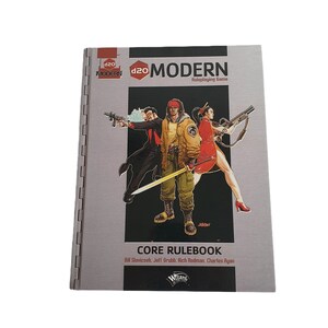 Op de afbeelding: Een grijs boek met de titel "d20 MODERN Roleplaying Game" en de ondertitel "CORE RULEBOOK". De omslag toont een illustratie van drie personen, twee mannen en een vrouw, in een moderne setting. Het boek is uitgegeven door Wizards of the Coast.