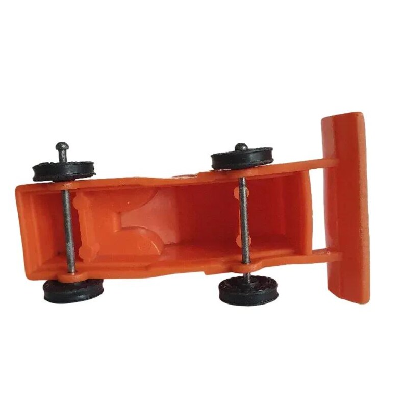 May include: An orange toy truck with black wheels and silver axles. The truck has a rectangular body and a flat front. The wheels are small and round. The toy is made of plastic.