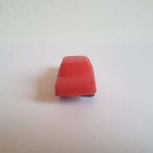 May include: A red toy car with a simple design. The car is made of plastic and has a smooth finish.