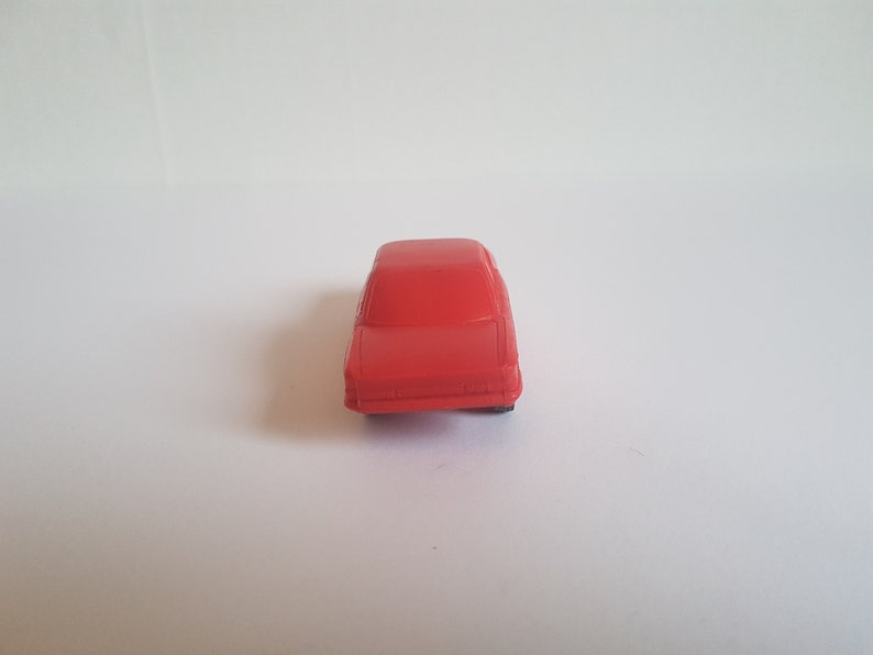 May include: A red toy car with a simple design. The car is made of plastic and has a smooth finish.