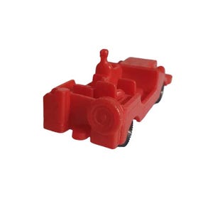 May include: A small, red toy car with a spare tire on the back. The miniature vehicle has a driver's seat and passenger seating. The wheels are black. The toy car is made of plastic.
